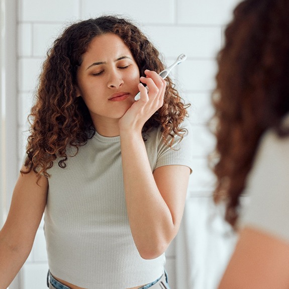 a woman brushing her teeth and experiencing pain